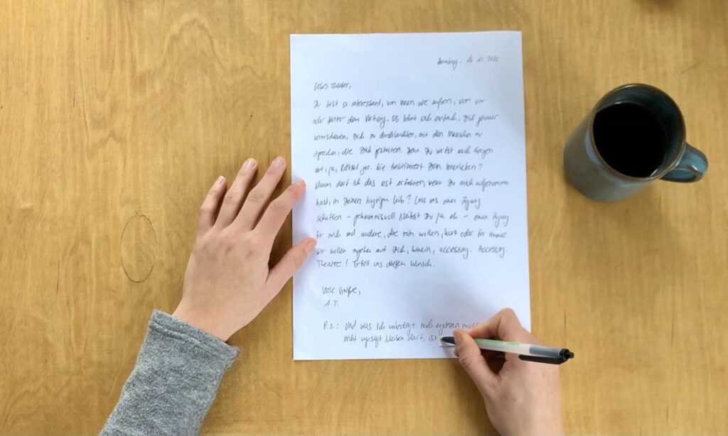 Eine Person schreibt mit einem Stift auf ein weißes Blatt Papier, welches auf einen Holztisch liegt