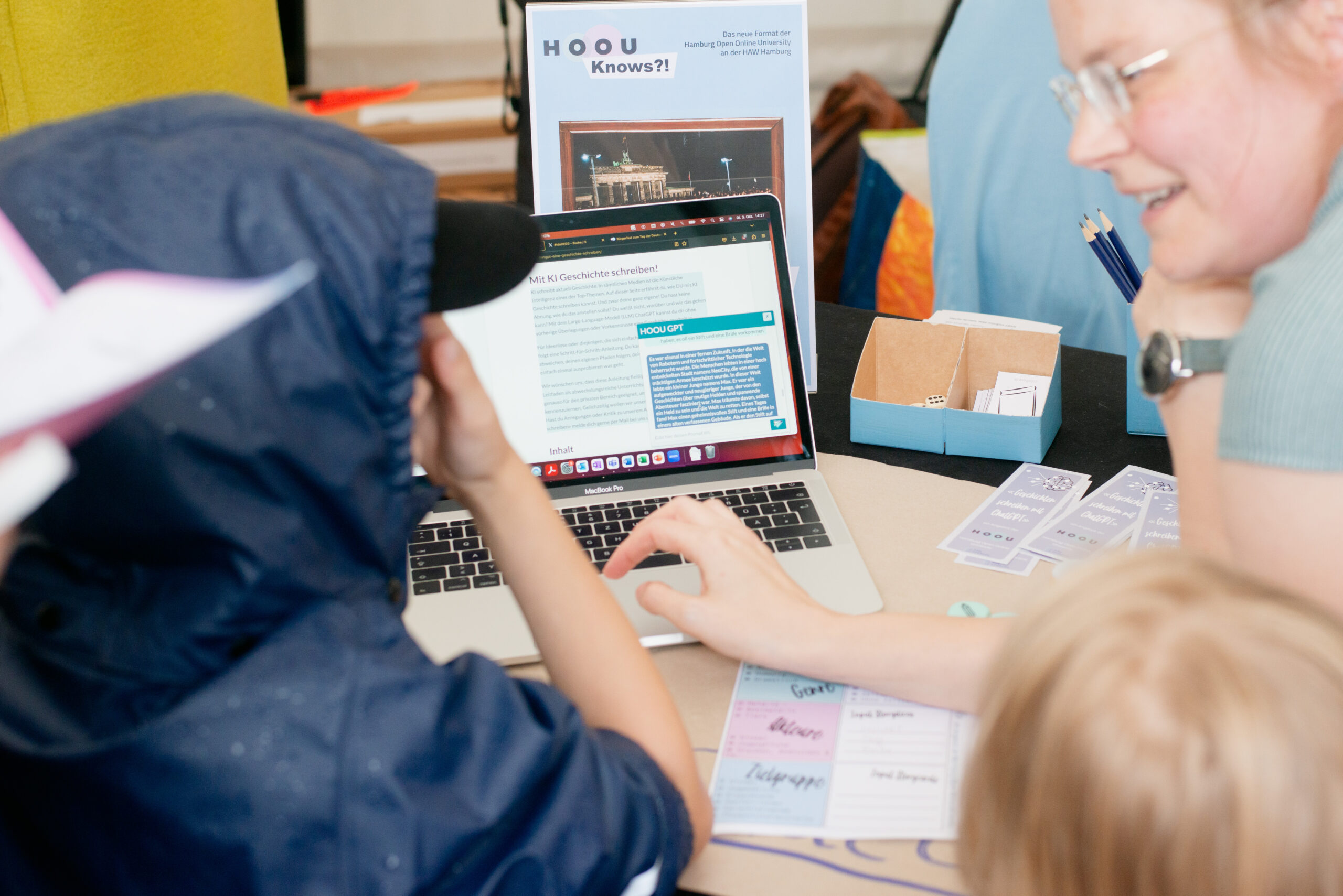 Das Bild zeigt Dr. Nicole Hagen und ein Kind. Nicole Hagen zeigt dem Kind ihr Lernangebot "Geschichte schreiben mit ChatGPT" auf einem Laptop.