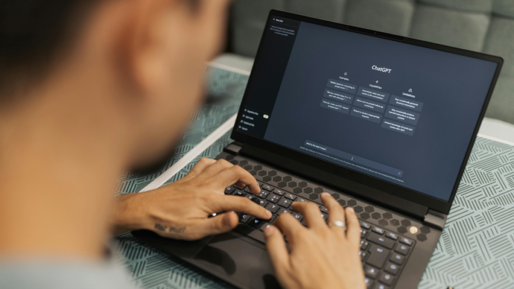 Das Bild zeigt eine Person vor einem Laptop. Auf diesem ist der KI-Chatbot ChatGPT zu sehen.