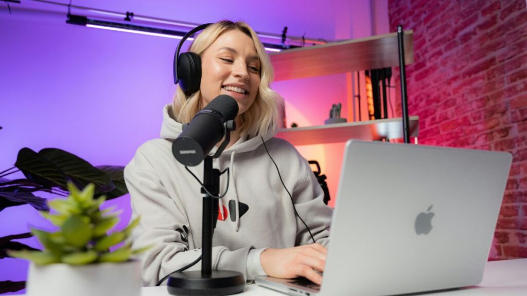 Eine Frau trägt Kopfhörer, hat ein Mikrofon und einen Laptop vor sich und spricht einen Podcast ein.