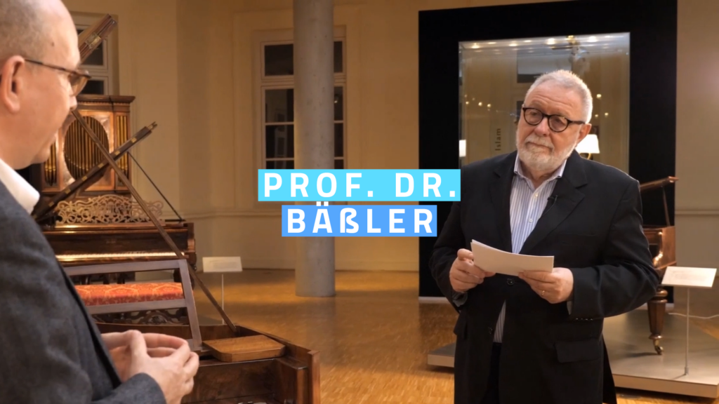 Prof. Dr. Bäßler steht vor historischen Klavieren