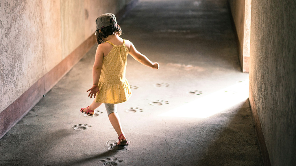 Das Bild zeigt ein tanzendes Mädchen, das einen Weg abläuft, auf dem Fußabdrücke im Beton zu sehen sind.