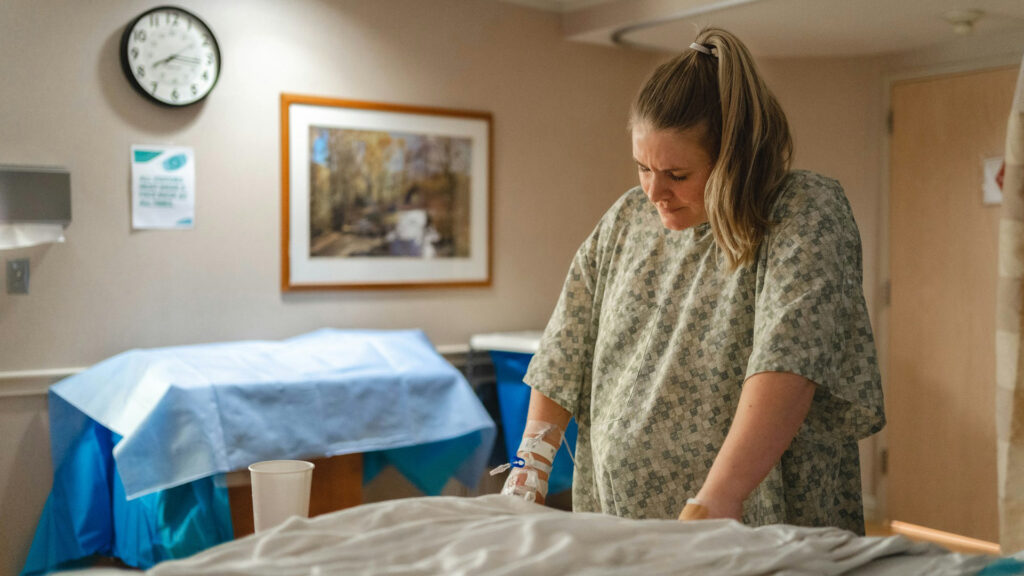 Das Bild zeigt eine hochschwangere Frau, die sich auf ein Krankenhausbett lehnt.