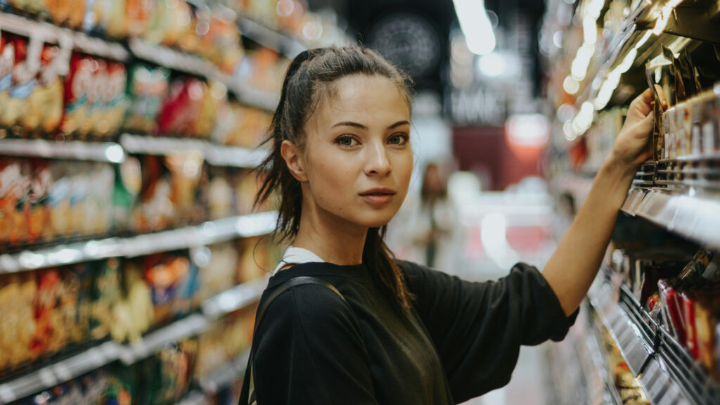 Eine Frau steht vor einem Supermarktregal und greift zu.