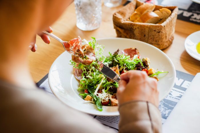 Jemand isst einen Salat. Zu sehen sind Besteck und ein gemischter Salat auf einem Holztisch