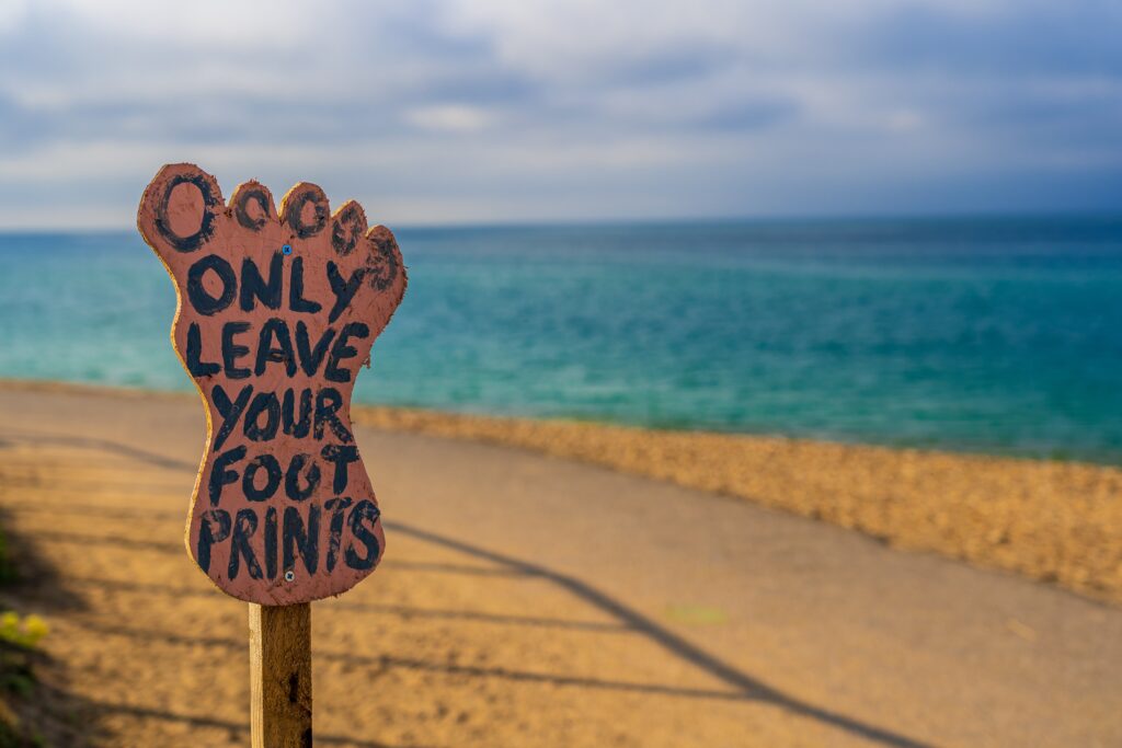 Ein Strandbild mit einem Fußabdruck aus Holz auf dem steht: Only leave your foot prints