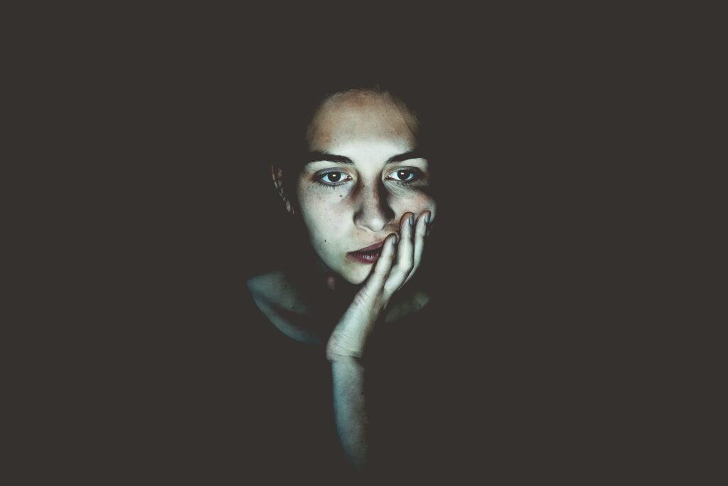 Eine Frau sitzt in einem dunklen Raum. Sie hat schwarze Haare und schwarze Kleidung an