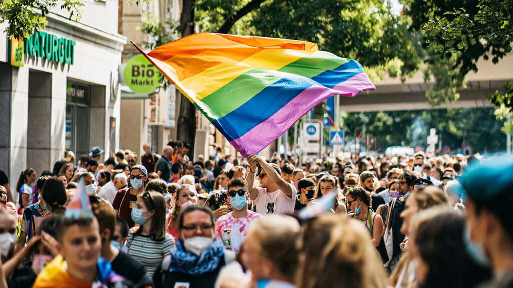 Das Bild zeigt eine Parade für Toleranz. In der Menschenmenge wird eine Regenbogenflagge geschwenkt.