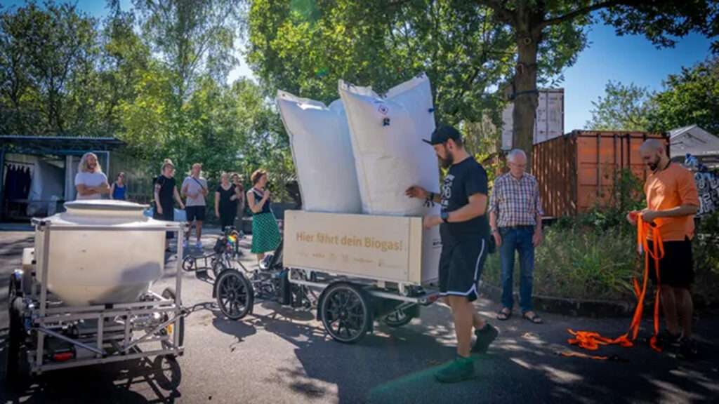 Das Bild zeigt Menschen, die Biogas in Säcken mit dem Rad transportieren.