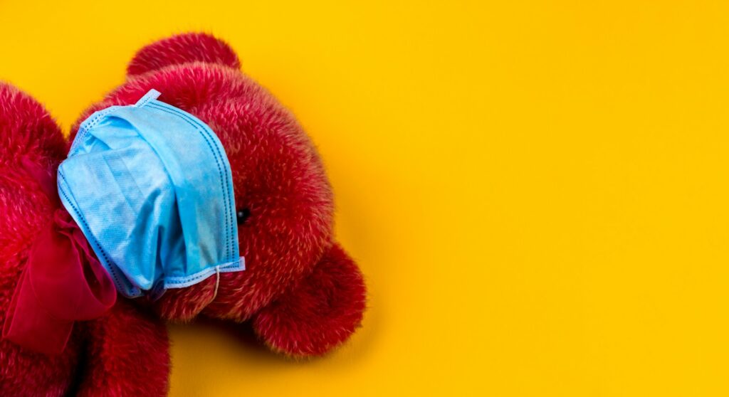 Auf dem Bild ist ein roter Teddybär mit Mundschutz zu sehen.